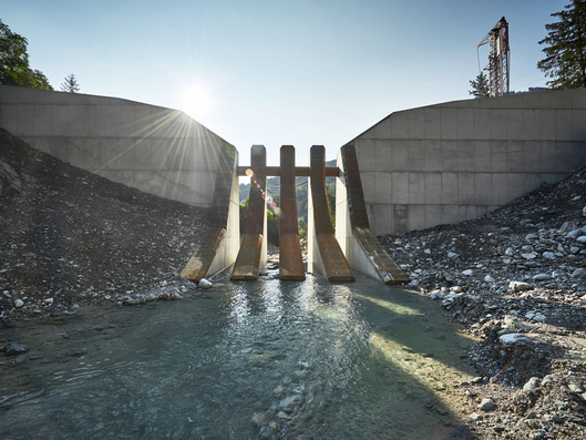 Front view of a torrent barrier during the day with the sun and an excavator in the background